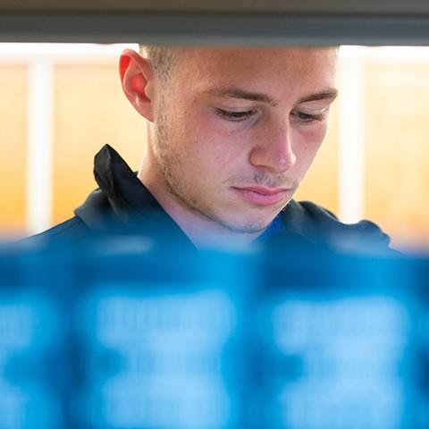 View of a student's face over a row of blue books as seen through a bookshelf